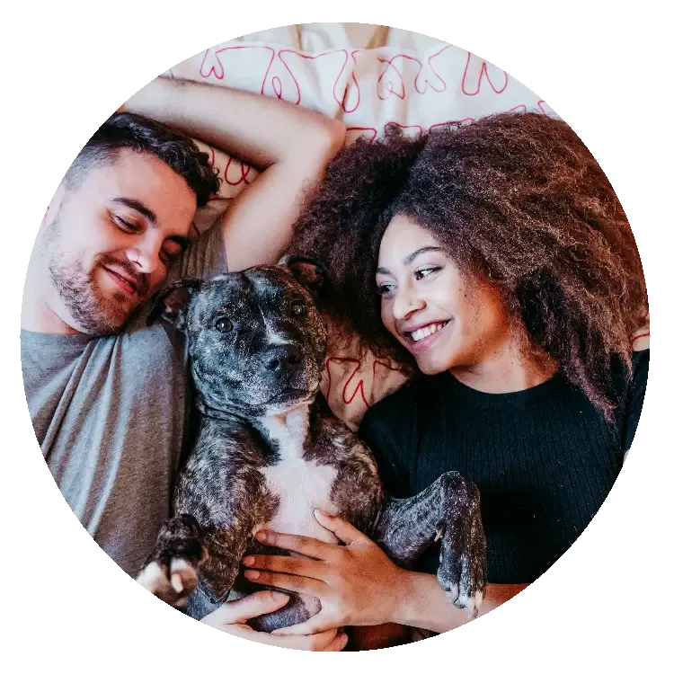 Two people lying beside a dog on a bed, with the dog centered between them.